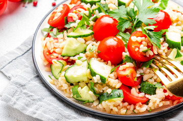 Bulgur tabbouleh salad with tomatoes, cucumbers and parsley. Traditional Middle Eastern dish. White table background, top view