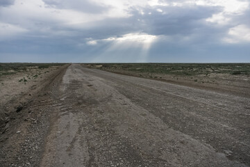Through a dense layer of clouds and clouds, the sun's rays break through in the desert steppe, in...