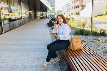 Lifestyle portrait of a stylish young businesswoman talking on cell phone, making call and standing on modern city street. Successful small business. Urban lifestyle concept.