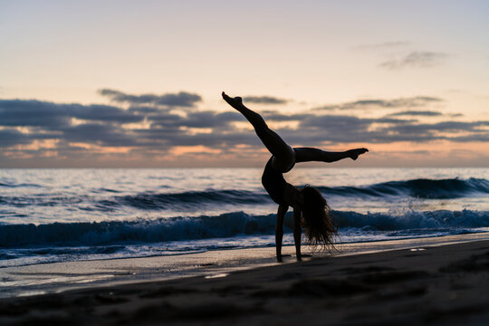 Silueta De Chica Realizando Movimientos De Gimnasia Y Baile Al Atardecer En Playa Paradisiaca