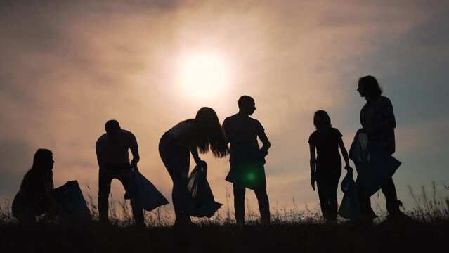 Teamwork.Silhouette of group of people clean up garbage at sunset in nature.Environmental pollution.Family cleaning plastic garbage in bag.People volunteers cleaning garbage in nature in summer park