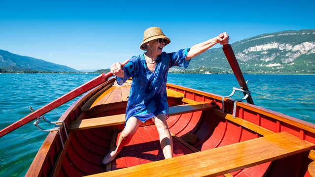 Femme avec un chapeau ramant dans une barque sur un lac en rigolant