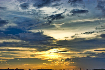 Dramatic sunset with vibrant clouds painting the sky in hues of gold, blue, and gray, casting a...