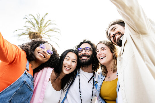 Low angle of a diverse group of friends standing and taking a selfie in the street. Low view of cheerful multiracial group of young hipsters taking a picture outside.