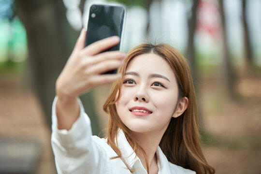 A young woman is taking pictures using her smartphone in a forested park.