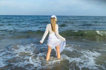 Fototapeta na wymiar Beautiful girl in the sea. The woman enters the sea. Blue ocean. Girl in a white cape. Beautiful woman on the beach. Summer vacation at sea. The girl loves the sea.