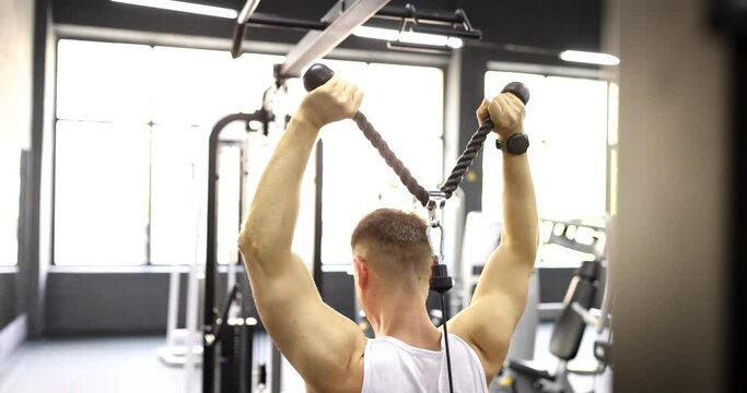Rear side view of man holding dumbbell lifting equipment behind back. Exercises for muscles of biceps and back