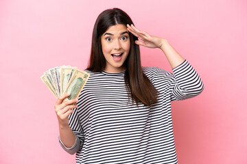 Young Brazilian woman taking a lot of money isolated on pink background with surprise expression