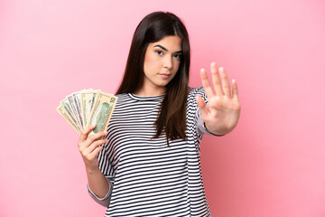 Young Brazilian woman taking a lot of money isolated on pink background making stop gesture