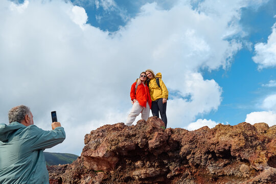 Hiking on tallest volcano in Continental Europe - Etna. Group of friends taking photo on the mountain peak of panoramic view of Mount Etna with cloudy sky in background.