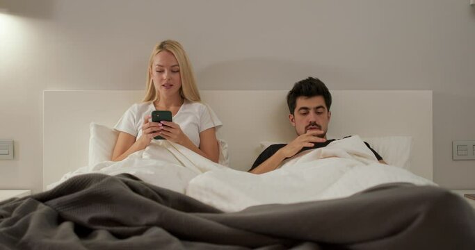 Couple of caucasian man and woman arguing, lying on bed in bedroom at home, Social distancing and self isolation in quarantine lockdown for Covid19. man grab, take woman's phone as he is jealous
