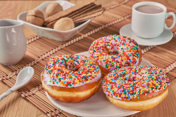 On a beige wooden table lies a beige bamboo napkin on which there is a plate with three donuts.