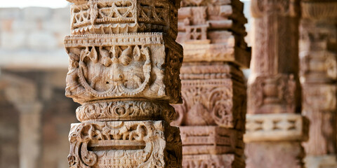 Stone columns with decorative bas relief of Qutb complex in South Delhi, India, close up pillars in ancient ruins of mosque landmark, popular touristic spot in New Delhi, ancient indian architecture