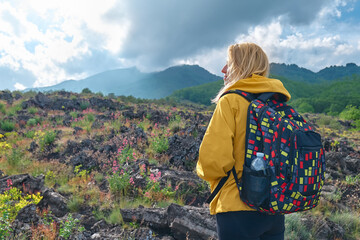 Hiking on tallest volcano in Continental Europe - Etna. Young woman in yellow raincoat standing on...