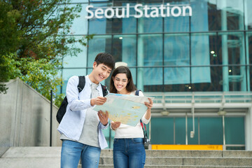  A couple dragging suitcases and looking at a map at a Korean train station
