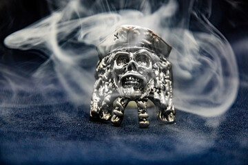 A ring in the form of a pirate skull shrouded in gray smoke on a dark background