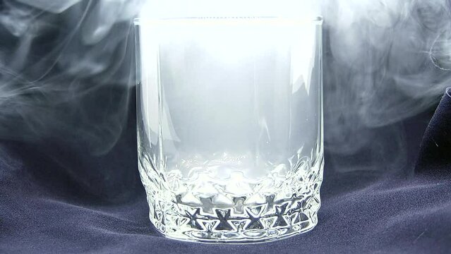 Gray smoke fills a transparent glass on a dark background in the video