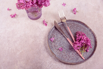 Beautiful table setting with lilac flowers and purple fabric on light gray background. Holidays decoration for romantic dinner in restaurant. Top view with copy space for text