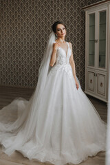 Fototapeta premium The brunette girl is preparing for the wedding. Portrait photo of a bride in a wedding dress with an elegant hairstyle and luxurious makeup, full-length photo