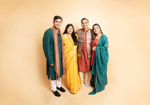 Happy indian family wearing traditional cloths standing isolated on beige background. Celebrating diwali festival, Occasion of wedding, Ethnic wear fashion.