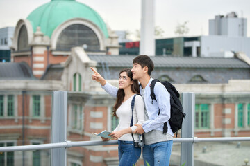 During the trip, a college student couple is looking for their way with a map at Seoul Station during the day.