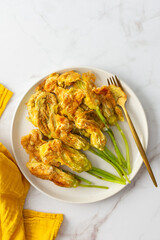 Fried zucchini flowers in batter, plate with zucchini flowers on marble background, top view