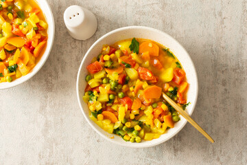 Minestrone soup from zucchini and tomato, onion and carrot, corn and peas with parsley, top view of soup plates, vegetarian soup