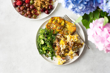 Healthy breakfast, scrambled eggs with fried mushrooms Chanterelles, salad with arugula, cucumbers and various seeds, fried zucchini pancakes, a plate with berries and a bouquet of hydrangeas