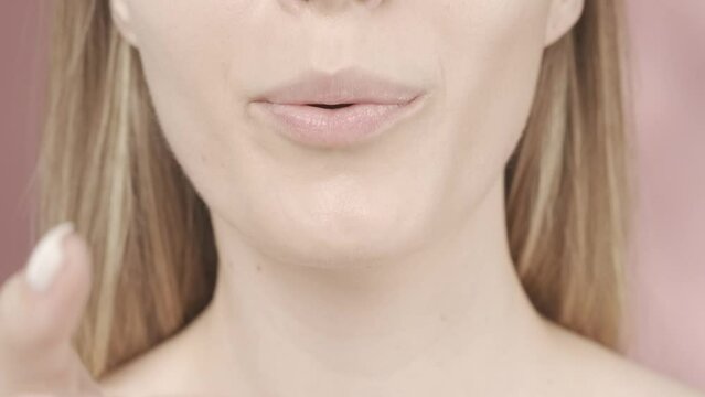 A woman puts her hand to her mouth and sends an air kiss. Woman's lips with natural pink gloss close up in the studio on a pink background. Slow motion. HDR BT2020 HLG Material.