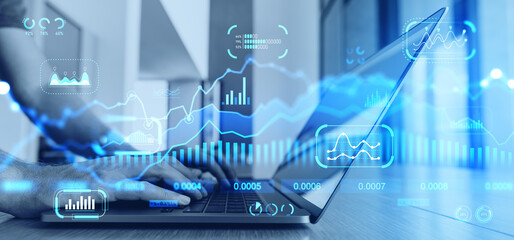 Man typing on laptop in office with digital financial charts