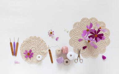 Summer needlework and craft. Process of crochet lace doily. Set of cotton yarn, hooks and bouquet of pink cosmea flowers on white table. DIY concept, handmade gifts. Top view, copy space, flat lay