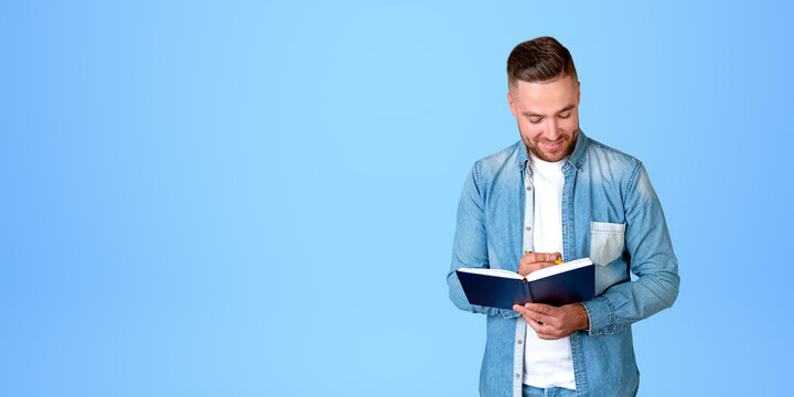 Man student taking notes smiling on empty blue background, copy space