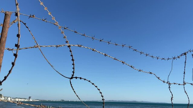 barbed wire barrier against the sea and blue sky background. barb wire fence over blue sky and sea