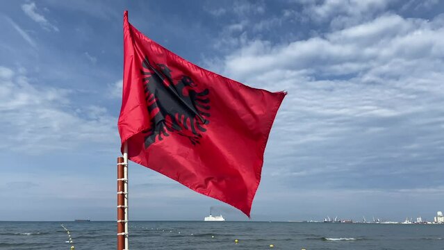 The red silk Albania Flag waves on blue sky background,  flag on a flagpole