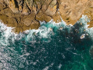 Aerial view of ocean waves crashing against the coastline on a sunny day
