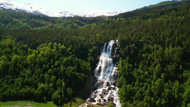 Drone landscape of Tvindefossen waterfall with a green forested hill view on a sunny day