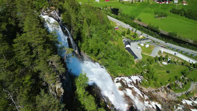 Drone landscape footage around Tvindefossen waterfall with a green forested on a sunny day