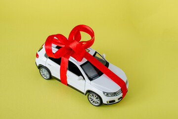 White model car with bow on a yellow background. Car as gift, surprise
