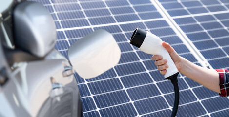 Hand with electric vehicles charging plug on a background of solar panel