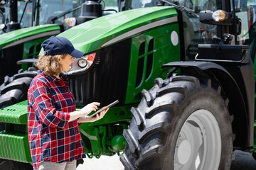 Woman farmer with a digital tablet on the background of an agricultural tractors.