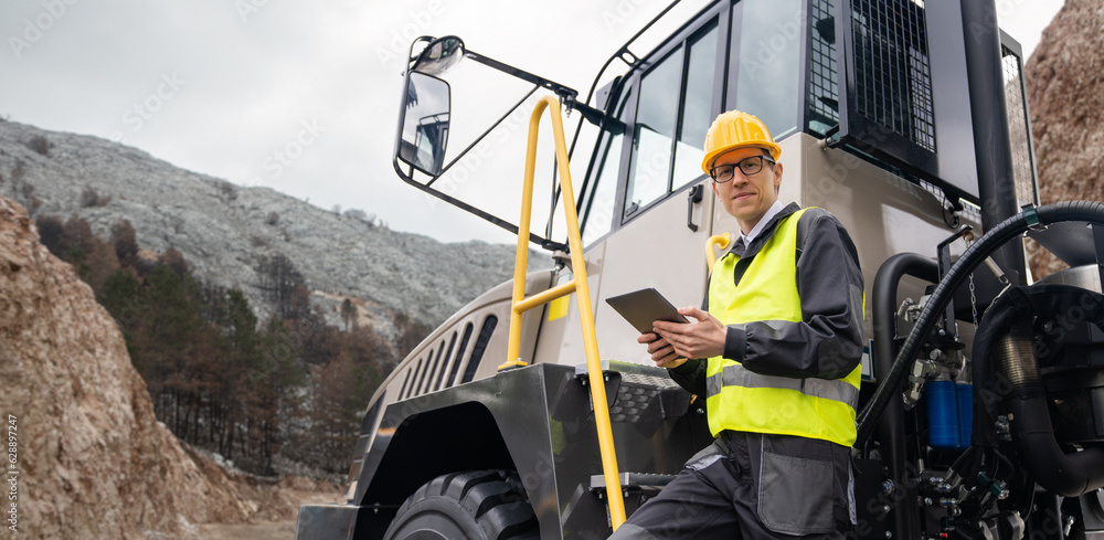 Poster engineer with tablet computer stands on the stairs to the cab of a truck