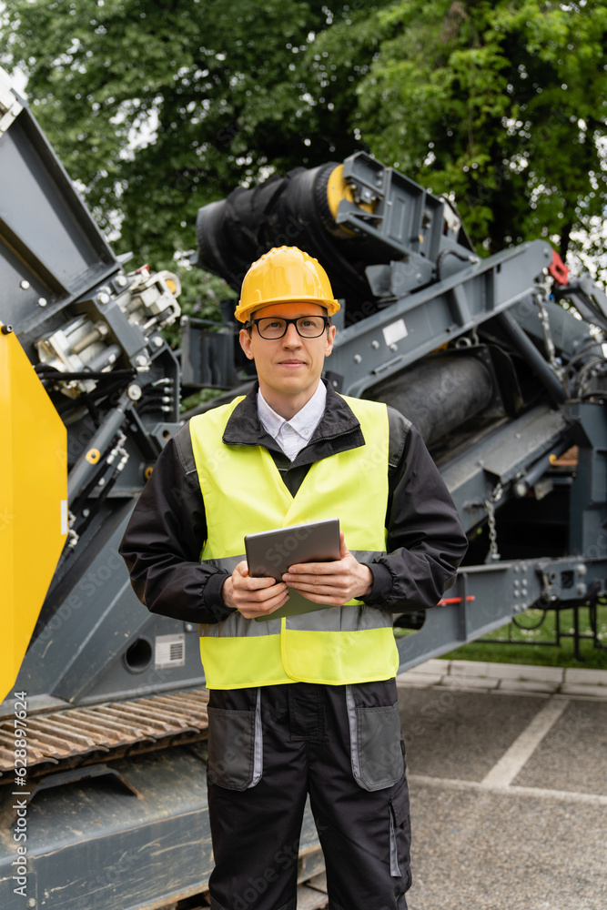 Poster engineer with digital tablet next to road construction machine