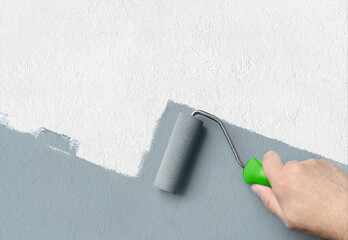 Man applying grey paint with roller brush on white wall, copy space