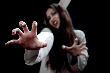 Beautiful black long hair woman with knife in head wearing white ghost spooky costume, standing with scary hand reaching out in dark background, going to celebrate Halloween party, play trick or treat - obrazy, fototapety, plakaty