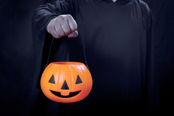 Halloween pumpkin in hand of man in spooky black costume standing in dark background, sorcerer...