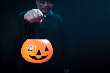 Halloween pumpkin in hand of man in spooky black costume standing in dark background, sorcerer...