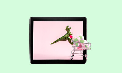 Dinosaur with shopping cart full of present boxes on digital tablet screen. Online sale and shopping concept. Place for text.