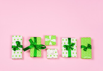 Green and white polka dot decorative gift boxes on pink background. Copy space.
