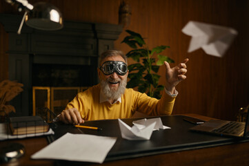 Funny overjoyed mature man wearing pilot goggles playing with origami plane