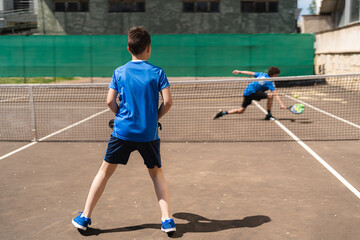Anonymous young boy playing padel with friend in daylight on sports ground